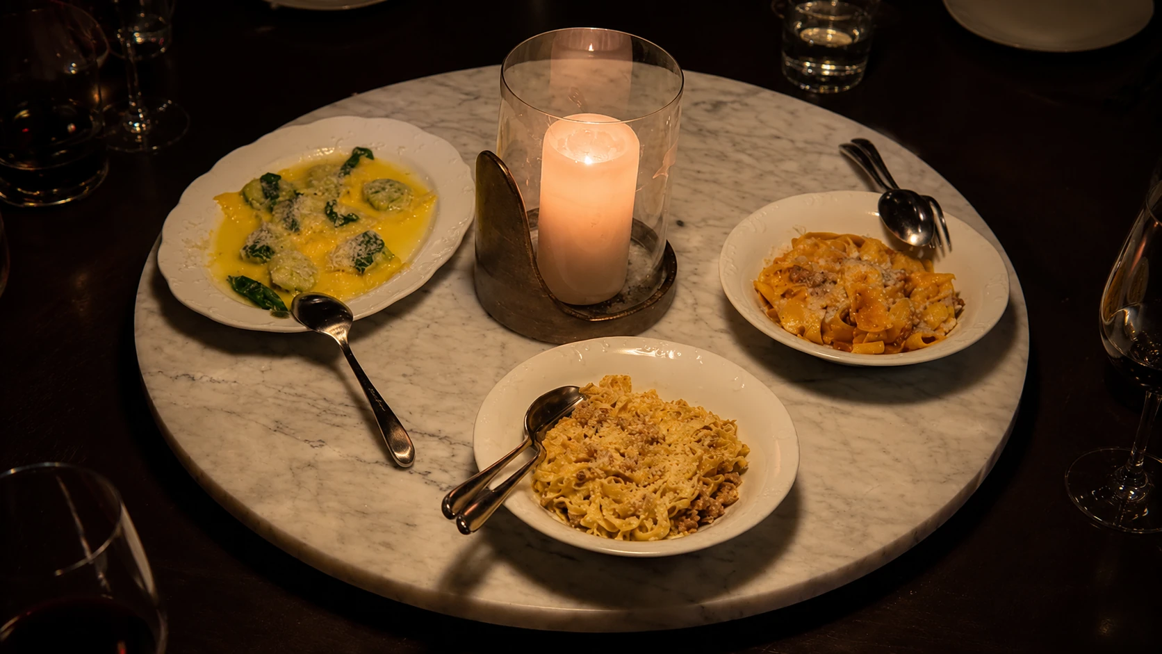 Three pasta dishes around a candlelit marble table at Tre Dita Chicago